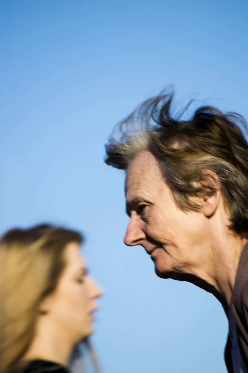 Windblown profile of an older woman passing a blurred younger woman against a blue sky